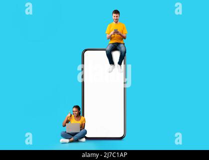 Couple sitting on white empty smartphone screen and using gadgets Stock Photo