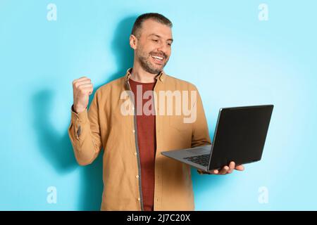 Joyful Man Using Laptop Shaking Fists On Blue Background Stock Photo