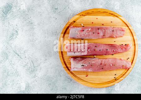 Pork tenderloin on a gray concrete background and board with vegetables and dill. Meat fillet on a cutting board. Stock Photo