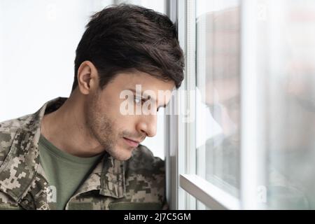 Portrait of depressed guy soldier looking through window at home Stock Photo