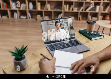 E-learning concept. Male student having online class via laptop, writing in notebook and taking notes, sitting at table Stock Photo