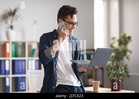 Young Businessman Talking On Mobile Phone And Using Laptop At Office Stock Photo