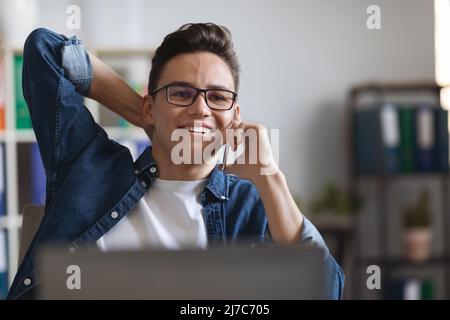 Handsome young guy in eyeglasses talking on phone at workplace in office Stock Photo