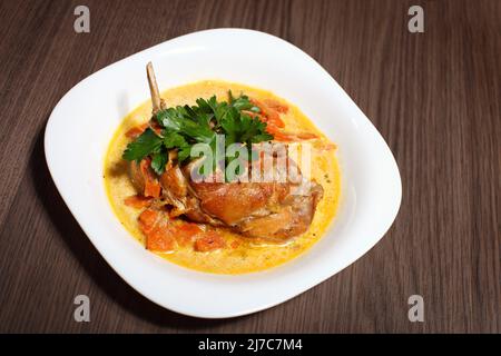 Plate with roasted rabbit leg and vegetable garnish. Stock Photo