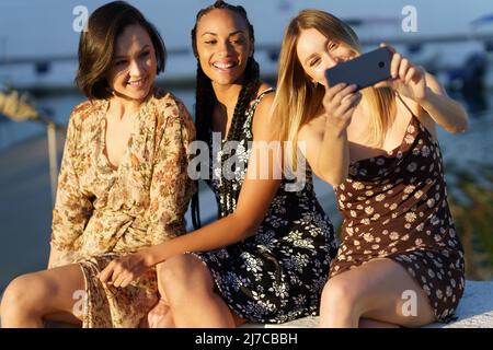 Cheerful diverse girlfriends taking selfie on smartphone in sunny day Stock Photo