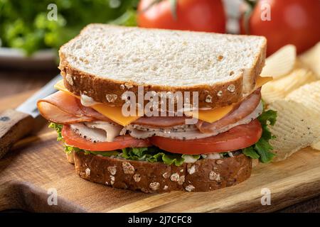 Sandwich made with turkey, ham, cheese, lettuce and tomato on whole grain bread Stock Photo