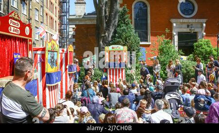 London, UK, 8th May 2022. Families watch the Punch and Judy shows with their children in beautiful sunshine. Puppeteers from across the country once again gather for the annual May Fayre and Puppet Festival, for the first time since 2019. It takes place at St Paul's Church (also called The Actor's Church), Covent Garden and includes a church service, procession, workshops, stalls and family fun. This year, it is also celebrating Mr Punch's 360th birthday. Stock Photo