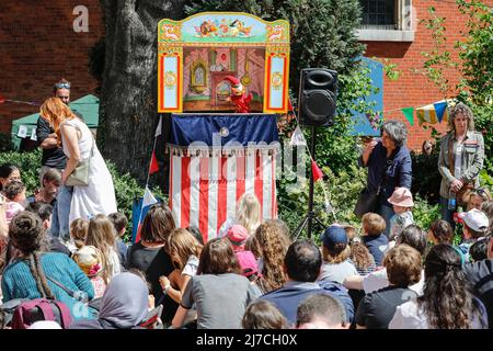London, UK, 8th May 2022. Families watch the Punch and Judy shows with their children in beautiful sunshine. Puppeteers from across the country once again gather for the annual May Fayre and Puppet Festival, for the first time since 2019. It takes place at St Paul's Church (also called The Actor's Church), Covent Garden and includes a church service, procession, workshops, stalls and family fun. This year, it is also celebrating Mr Punch's 360th birthday. Stock Photo