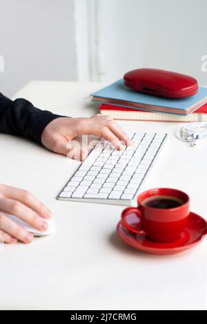 Man hands in lay on keyboard and mouse with red cup of coffee, notebooks, headhones and glasses case on white table Stock Photo