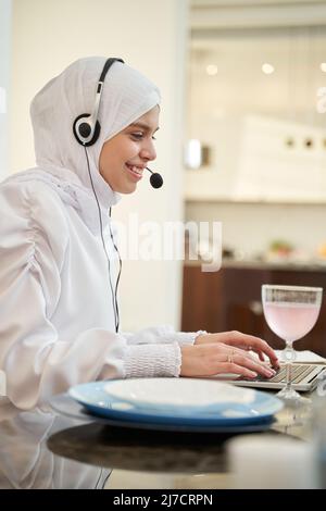 Cheerful Muslim woman working on laptop at home Stock Photo