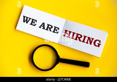 We are hiring text on notepad magnifying glass on yellow background. Employment concept Stock Photo