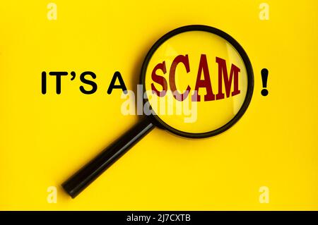 It's a scam text on yellow cover with magnifying glass. Scamming and fraud concept Stock Photo