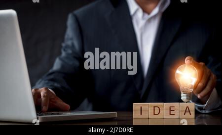 Hand man holding light bulb with text i d e a. Innovation idea and knowledge concept. Hand of businessman holding light bulb with laptop Stock Photo