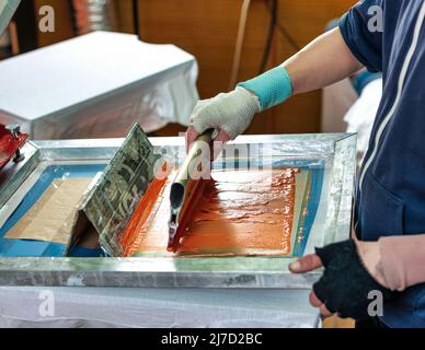 silkscreen printing. male hand with a squeegee. serigraphy production selective focus photo. printing images on clothes by silk screen method in a des Stock Photo
