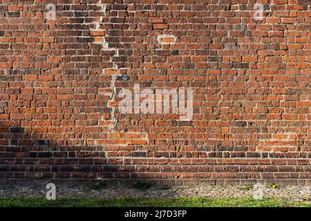 Old brick wall of a traditional building. A big crack in the house was repaired. Red bricks background texture. Abstract backdrop of an old facade. Stock Photo