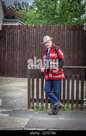 A man wearring western wear and hat standing in front of wooden fence. Stock Photo