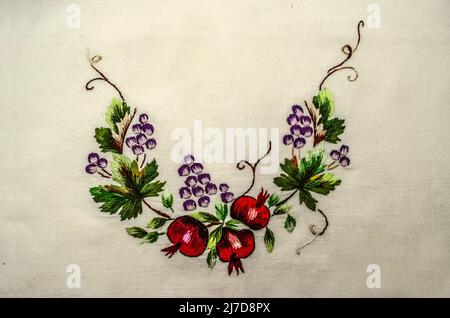 Yerevan, Armenia, April 04, 2022: Embroidered bouquet of red pomegranate fruits with small leaves ahd clusters of purple grapes  on curved branches wi Stock Photo
