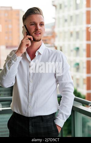 Young executive man talking on the mobile phone while standing on a balcony. Stock Photo