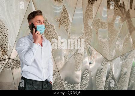 Executive man using a face mask while talking on the mobile phone outside the office building. Stock Photo