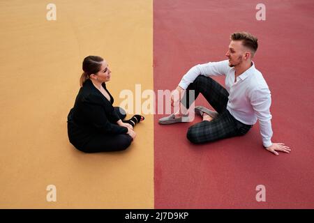 Two business people talking while sitting on floor outdoors. Stock Photo