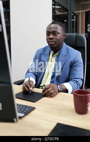 African serious designer concentrating on his work at table with computer using graphic tablet Stock Photo