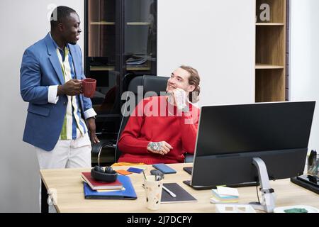 Two multiethnic colleagues talking to each other during work day at office Stock Photo