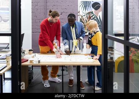 Group of architects standing at table and working over blueprint in team, they discussing new construction project Stock Photo