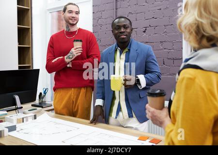 Two businessmen standing with coffee and talking to their colleague during teamwork at office, they working over new business project Stock Photo