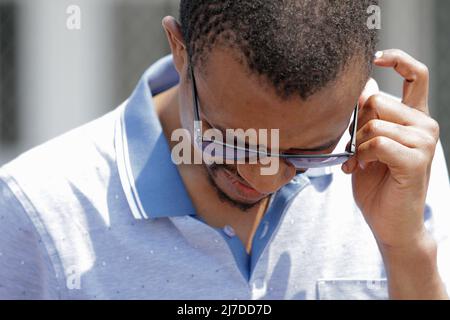 Man in deep concentration, looking down, scratching head, wearing sunglasses and a blue golf shirt. Stock Photo