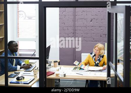 Designers sitting at table at modern office working on computer and with colour palette for future project Stock Photo