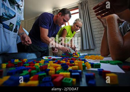 Students gathered around a table at the GSB team-building event, building LEGO structures using specific clues Stock Photo