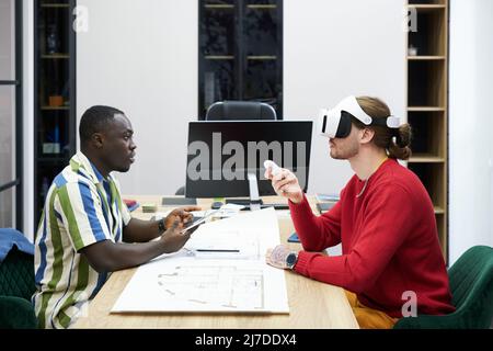 Business colleagues sitting at table opposite each othe and using virtual reality goggles at their work at office Stock Photo