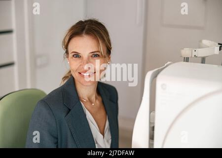 Smiling woman patient awaits a vision test at opticians shop or ophthalmology clinic Stock Photo