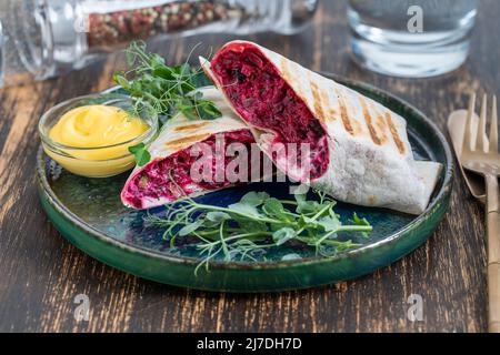 Vegan burrito. Sliced up raw food wrap with red beetroot, feta cheese, prunes, dill and cream sauce with pea microgreens on a plate. Close up Stock Photo