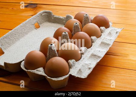 Chicken eggs in a package on the table. Brown chicken eggs in a recycled paper box on a wooden background. Natural eco-friendly healthy products. Lots Stock Photo