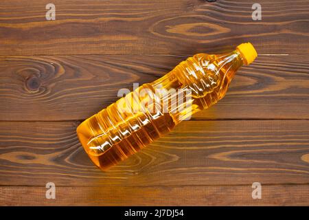 Oil in a bottle on the table. Olive oil in a plastic bottle with a yellow cap lies on brown wooden boards. A bottle of sunflower oil in the sun. Close Stock Photo