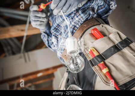 Electrician Installing New Light Point Inside a House. Preparing Light Bulb Close Up. Residential Electric Systems. Industrial Theme. Stock Photo