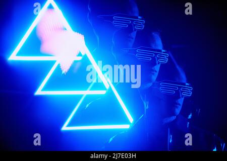 Cool boy in modern fashionable wire goggles standing in light of neon triangle sign Stock Photo