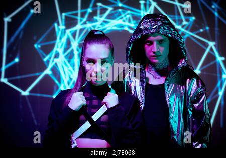 Portrait of serious young people from alternative world standing against neon lines background Stock Photo