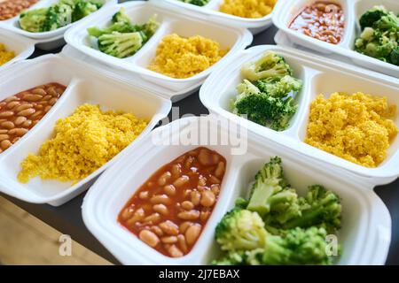 Part of table served with steamed broccoli, kasha and boiled beans in white plastic containers prepared for homeless people Stock Photo