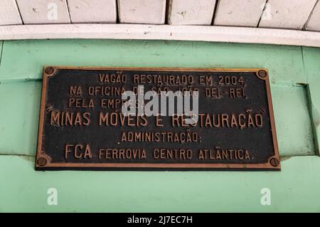 Metal information sign saying: "Passenger car restored in 2004 at Sao Joao Del Rei workshops by Minas Moveis e Restauracao shop. Admin: FCA railway". Stock Photo