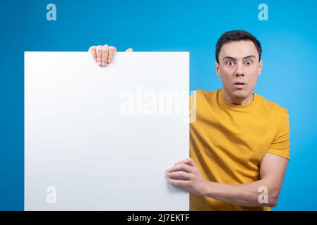 Startled guy showing white banner on blue background Stock Photo