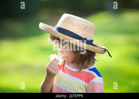 Portrait of a cute child boy in straw hat smelling plumeria flower. Close up caucasian kids face. Closeup head of funny kid. Stock Photo