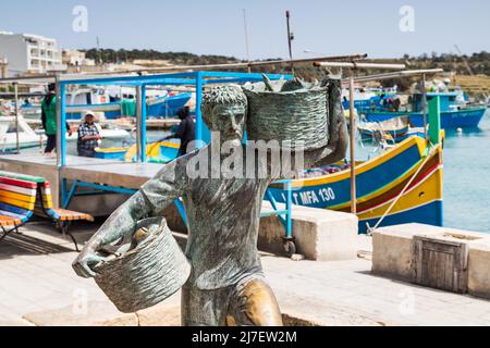 Fisherman statue in Marsaxlokk harbour seen in Malta during April 2022 carrying two baskets of fish from a boat. Stock Photo