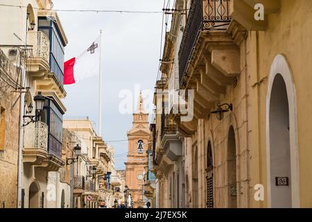 Malta flag flying high above a street in Mellieha, Malta in May 2022. Stock Photo