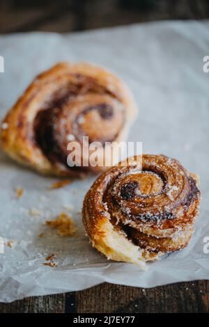 Two sugary cinnamon rolls on a baking parchment Stock Photo
