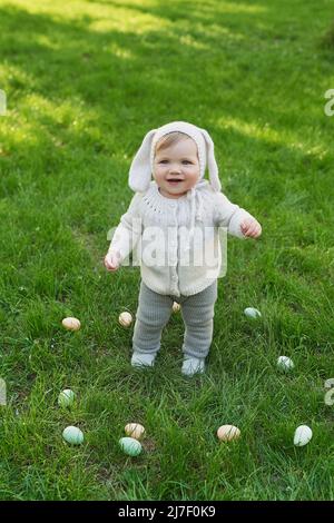 Easter Bunny baby boy. Egg hunting. Cute child in hat with ears and eggs on grass. Stock Photo