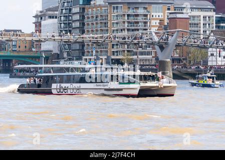 Uber Boat, Thames Clippers, named Venus Clipper, passing under Millennium Bridge with people crossing over the River Thames. Police launch Stock Photo