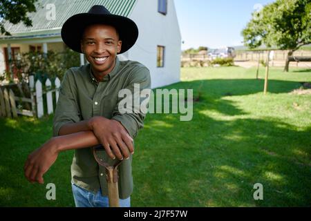 Mixed race male farmer standing in green field leaning on pitch fork  Stock Photo