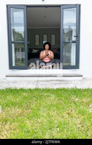 Full length of african american mid adult woman with eyes closed mediating while sitting at entrance Stock Photo